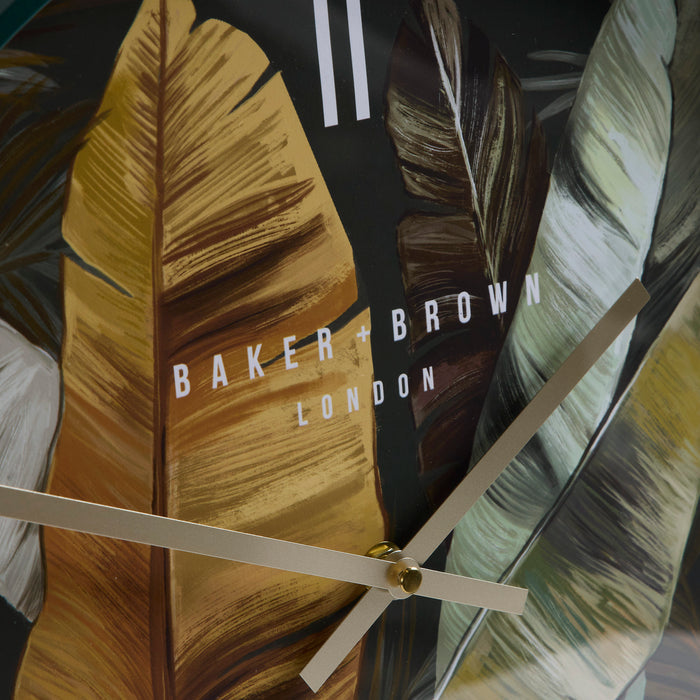Close-up of a Baker + Brown London wall clock featuring a tropical leaf pattern in gold, brown, black, and white, with minimalist beige hands.