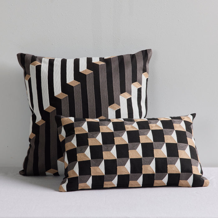 Two decorative throw pillows with geometric 3D cube patterns in black, white, and beige, displayed against a light gray wall.