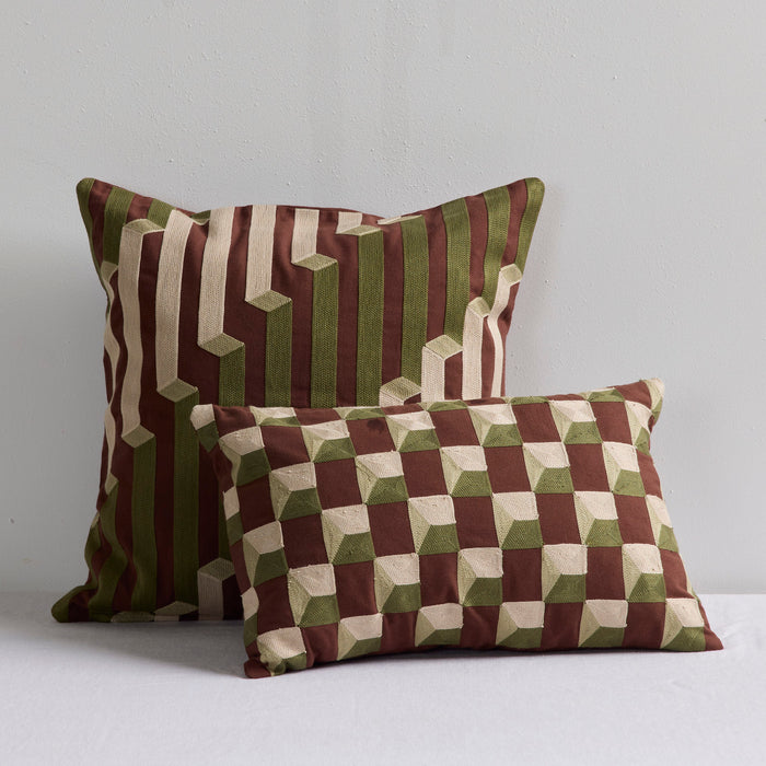 Two decorative throw pillows with geometric 3D cube patterns in brown, olive green, and cream, displayed against a neutral light gray background.