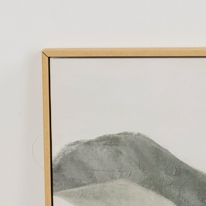 A close-up of a framed minimalist art print featuring a textured gray mountain on a white background, enclosed in a light natural wood frame against a white wall.