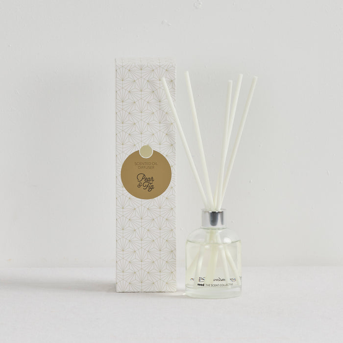 The Scent Collective Diffuser - Pear and Fig, clear glass reed diffuser with white reeds beside patterned packaging