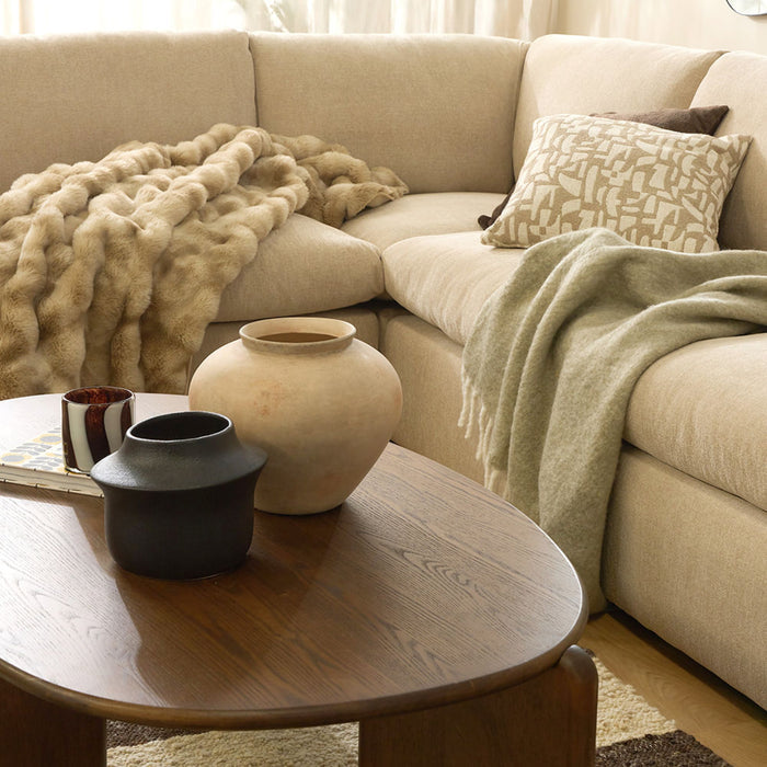 Beige sectional sofa with decorative pillows and a blanket, accompanied by a wooden coffee table with vases.