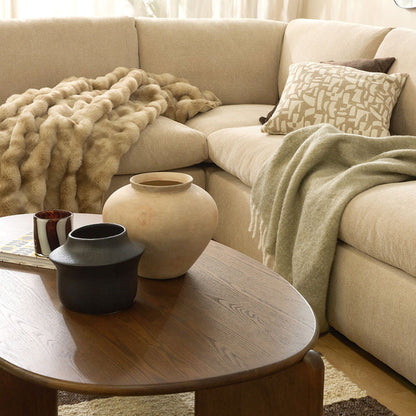 Beige sectional sofa with decorative pillows and a blanket, accompanied by a wooden coffee table with vases.