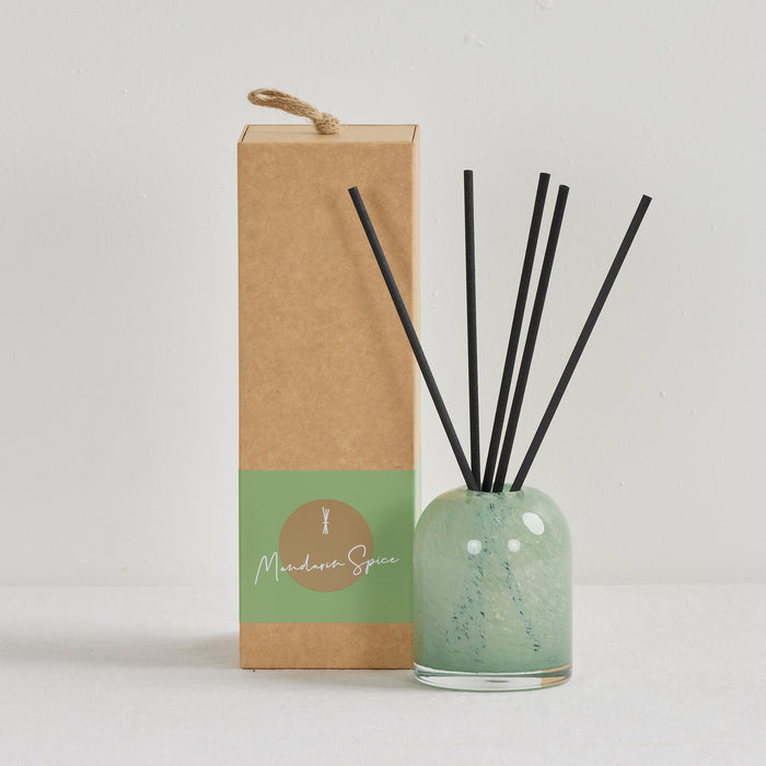 Aurora Diffuser - Mandarin Spice reed diffuser in a soft green glass vessel with black reeds beside kraft gift box