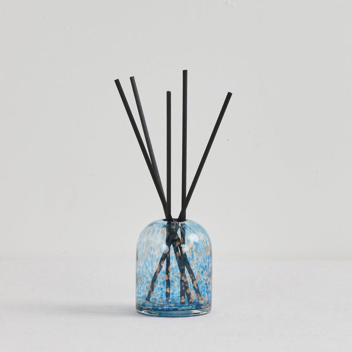 Aurora Diffuser - Sea Mist reed diffuser in a mottled blue and gold glass vessel with black reeds