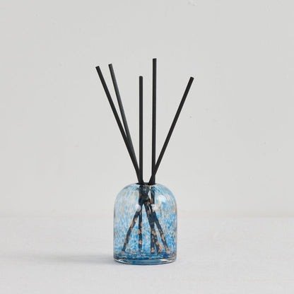 Aurora Diffuser - Sea Mist reed diffuser in a mottled blue and gold glass vessel with black reeds