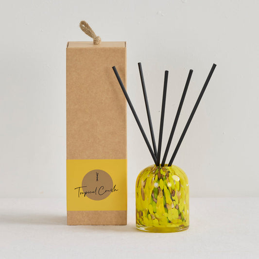 Aurora Diffuser - Tropical Crush reed diffuser in a mottled yellow glass vessel with black reeds beside kraft gift box