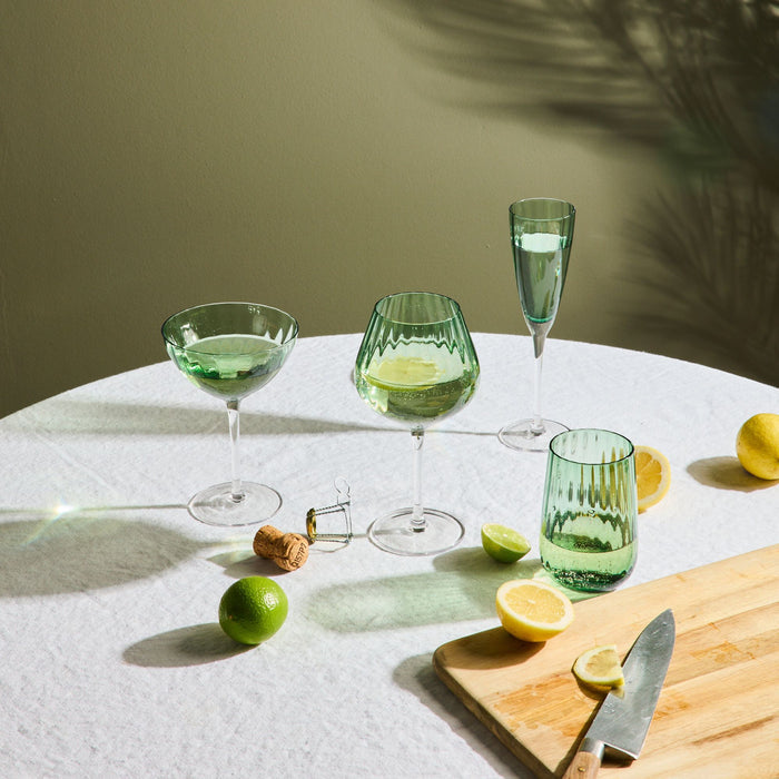 Green glassware on a table with lemons and a knife, against a neutral background