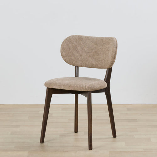 Beige upholstered chair with wooden legs on a light wooden floor and white wall background