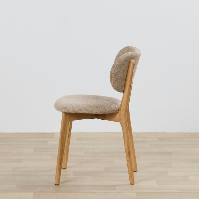 Chair with beige cushioned seat and backrest on a wooden floor with a light gray background