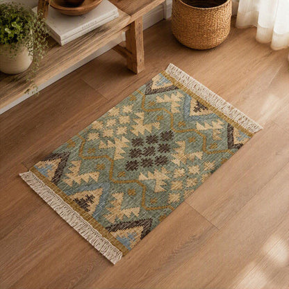 A rectangular woven area rug with a geometric Southwestern-style pattern in muted blue, beige, brown, and mustard tones, finished with cream fringe on both ends, shown on a light wood floor in a styled room setting.
