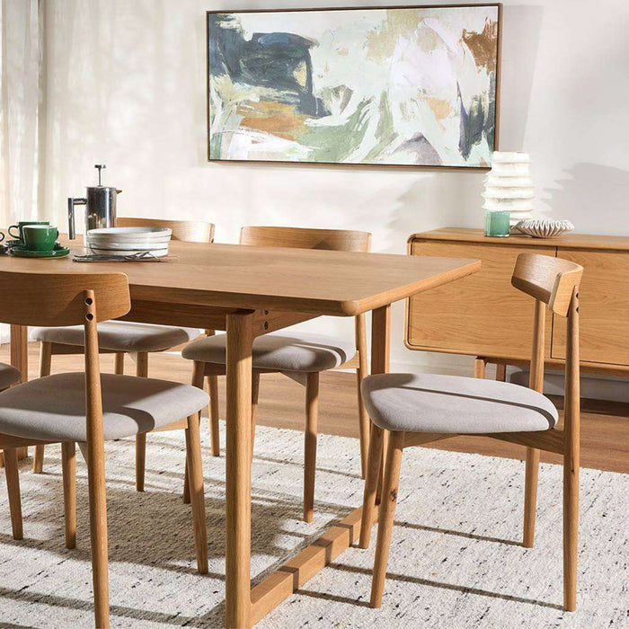 A mid-century modern wooden dining table set with six matching chairs featuring light gray upholstered seats, styled in a bright dining room next to a wooden sideboard.