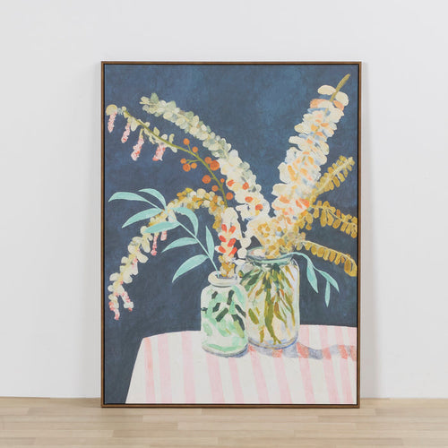 Framed artwork of flowers in jars on a striped tablecloth against a white wall.