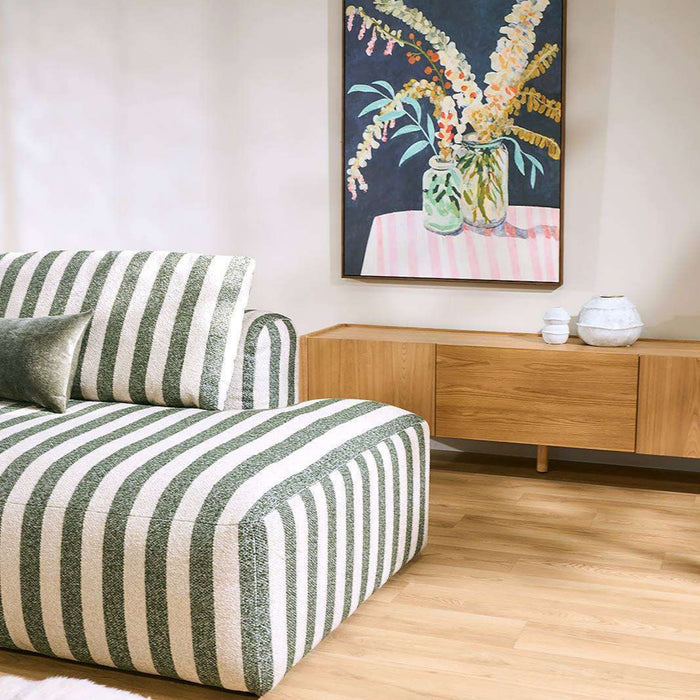 A modern armchair with vertical green and off-white stripes, styled in a minimalist living room next to a light wood sideboard and a framed floral painting.