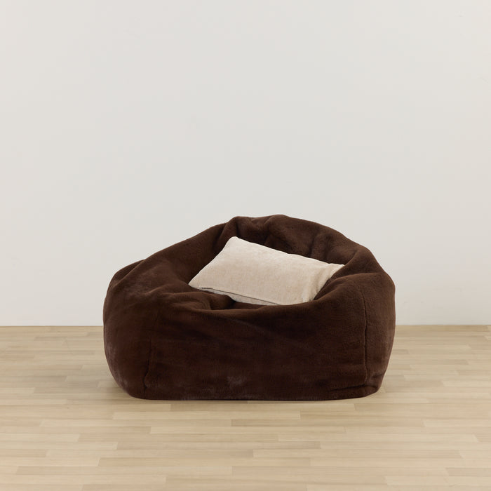 Brown bean bag chair with a beige pillow on a light wooden floor and white wall background