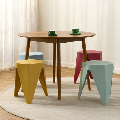 A round wooden dining table surrounded by four colorful geometric stools in yellow, light blue, red, and mint green, set on a round rug in a bright room with white curtains.