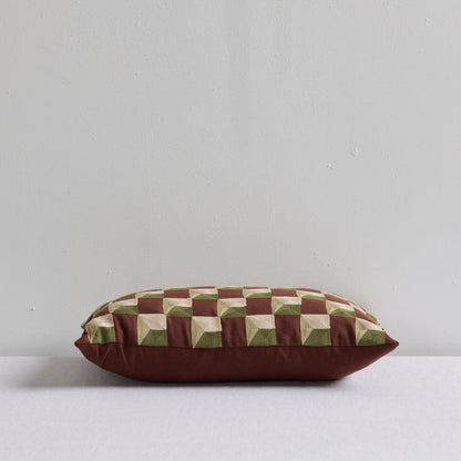 A rectangular throw pillow with a brown and olive green geometric cube pattern on top and a solid dark brown base, displayed against a light gray wall.