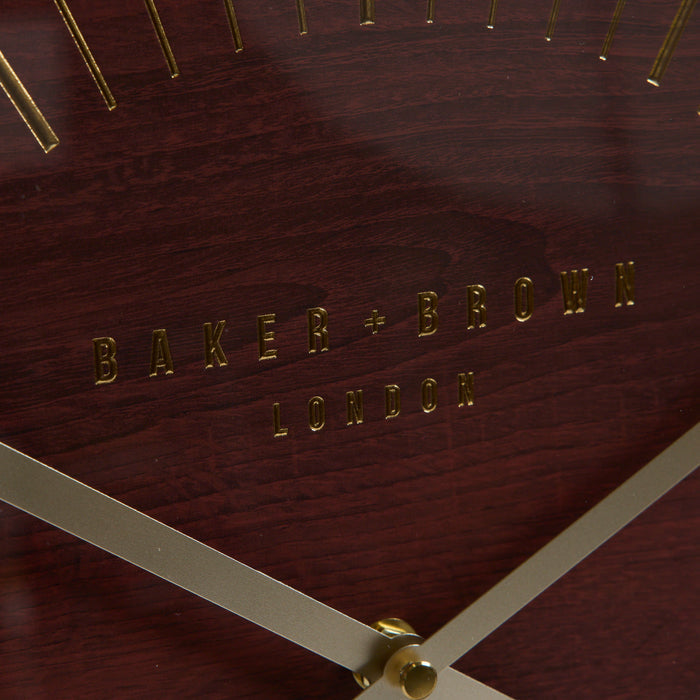 Close-up of a Baker + Brown London wall clock face showing a dark reddish-brown wood grain background with gold-tone lettering and clock hands.