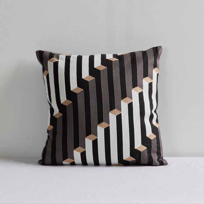 A square throw pillow with a modern geometric pattern of black, white, and gray vertical stripes accented by small beige 3D cube shapes, set against a plain light gray background.