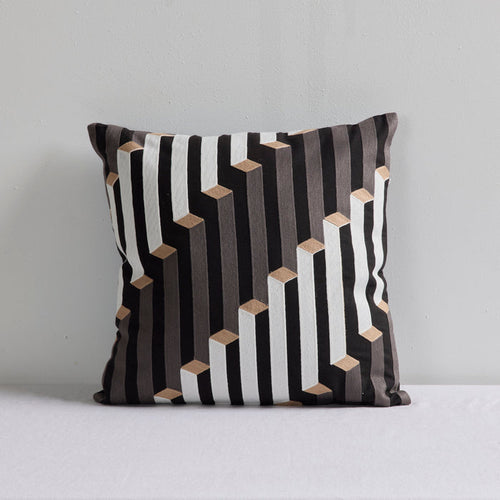 A square throw pillow with a modern geometric pattern of black, white, and gray vertical stripes accented by small beige 3D cube shapes, set against a plain light gray background.