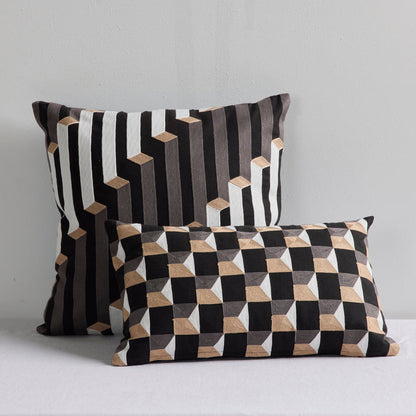 Two decorative throw pillows with geometric 3D cube patterns in black, white, and beige, displayed against a light gray wall.
