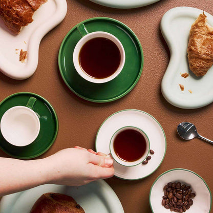 Mesa Coffee Cup & Saucer - Green glossy coffee cup and saucer styled with pastries and dinnerware on a brown table.