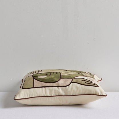 A square decorative throw pillow with an abstract line-art design in olive green, beige, and dark brown, resting on a white surface against a light gray wall.