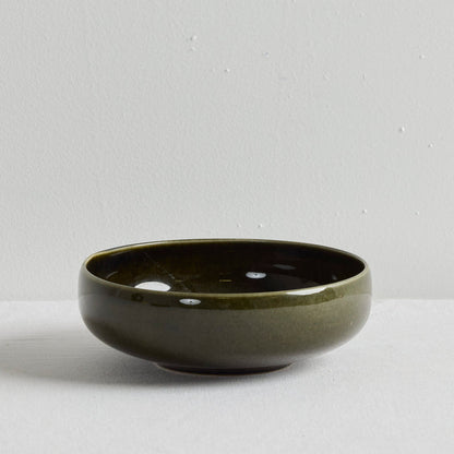 A small round ceramic bowl with a glossy dark olive green glaze, set against a neutral light gray background.