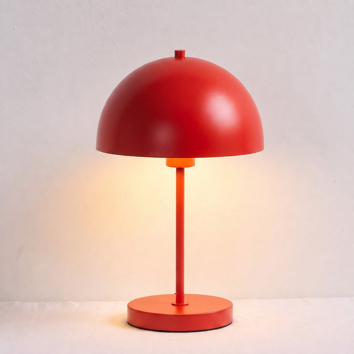 A modern mushroom-shaped table lamp with a glossy red dome shade, matching red stem, and round red base, shown lit against a light neutral background.