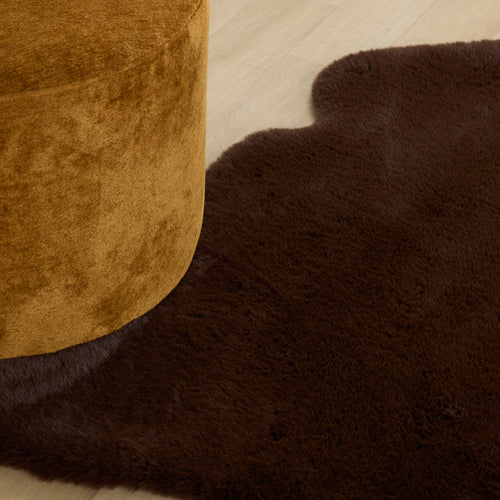 Brown textured ottoman and rug on a light wooden floor