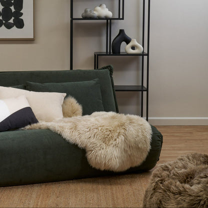 Sheepskin in Mink, draped over a green couch.