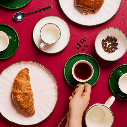 Soma Coffee Cup & Saucer - White/Green arranged with coffee, pastries and green-rimmed dinnerware on a red table.