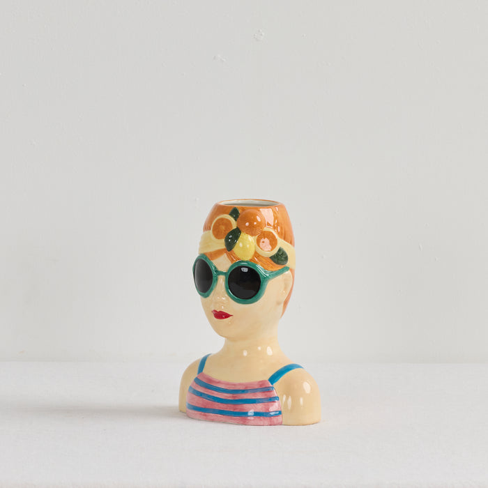 Vase shaped like a woman's bust with sunglasses and floral headband on a white background