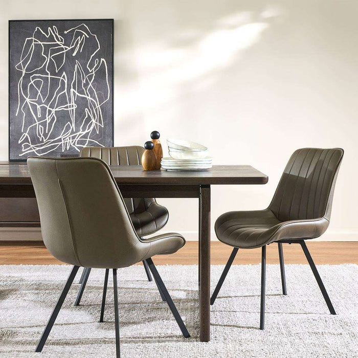A dining room scene with a dark wood table and three upholstered chairs in a taupe-brown color, set on a light rug against a beige wall with a framed abstract print.