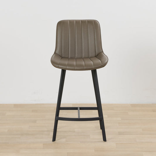 A single bar stool with a curved, vertically ribbed upholstered seat in taupe-brown faux leather and a black metal frame, set against a plain white wall and light wood floor.