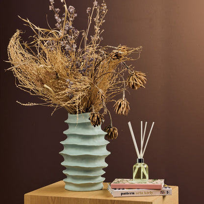 The Scent Collective Diffuser - Jasmine and Magnolia with pale yellow oil and white reeds beside dried flowers