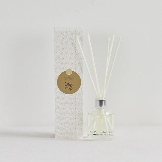 The Scent Collective Diffuser - Pear and Fig, clear glass reed diffuser with white reeds beside patterned packaging