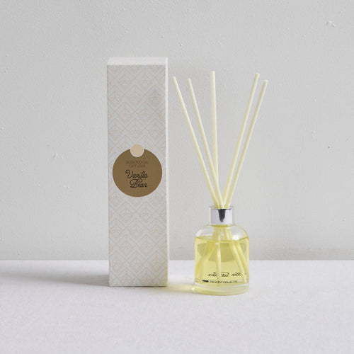 The Scent Collective Diffuser - Vanilla Bean, clear glass reed diffuser with pale yellow oil beside patterned packaging