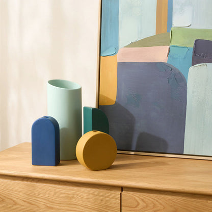 Colorful geometric vases on a wooden surface with a abstract painting in the background
