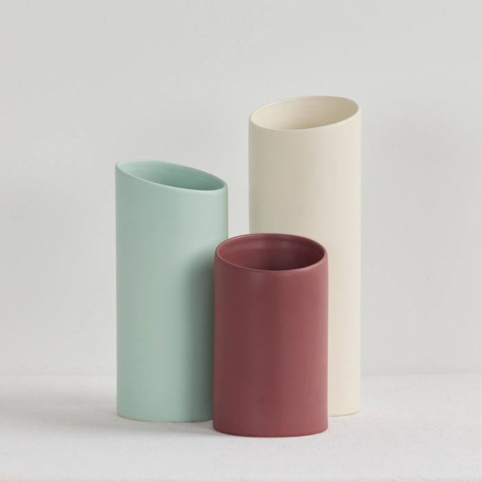 Three cylindrical vases in green, pink, and beige on a light gray background