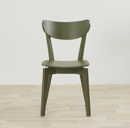 An olive green molded wood dining chair with a curved backrest and tapered legs, set against a minimalist white wall and light wood plank floor.