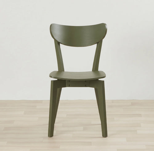 An olive green molded wood dining chair with a curved backrest and tapered legs, set against a minimalist white wall and light wood plank floor.